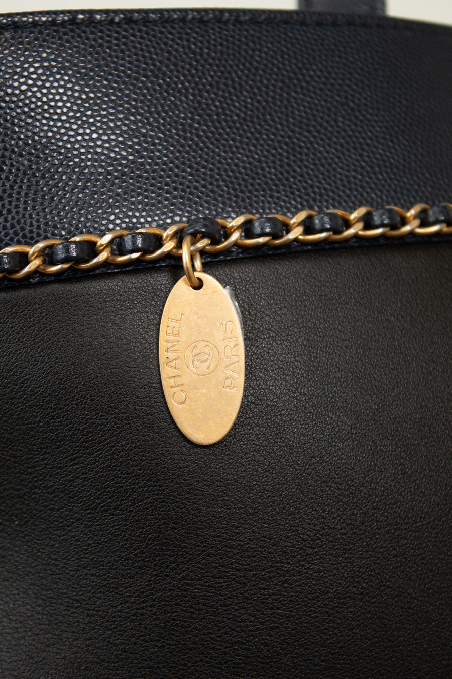 Close-up of a black leather handbag with a gold chain and tag, featuring the Chanel logo.