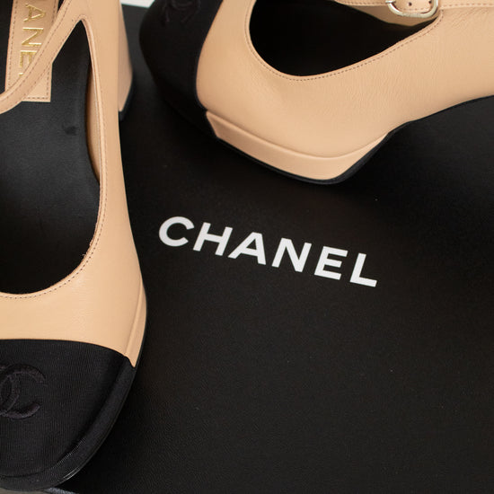 Beige and black Chanel high-heeled shoes on a black box with the Chanel logo.