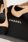 Beige and black Chanel high-heeled shoes on a black box with the Chanel logo.