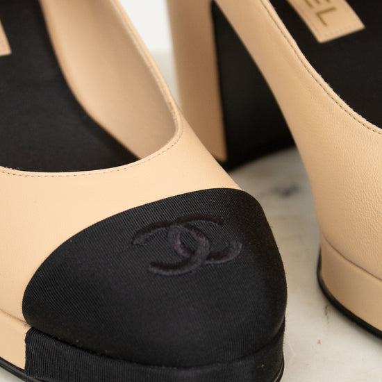 Close-up of beige high-heeled shoes with black featuring Chanel logo on a light background.