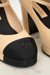 Close-up of beige high-heeled shoes with black featuring Chanel logo on a light background.