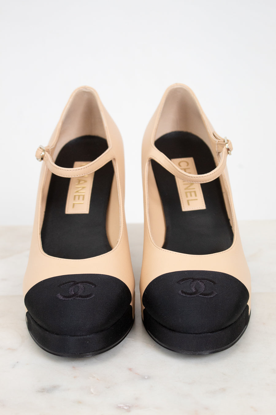 Pair of beige high-heeled shoes with black details on a light background