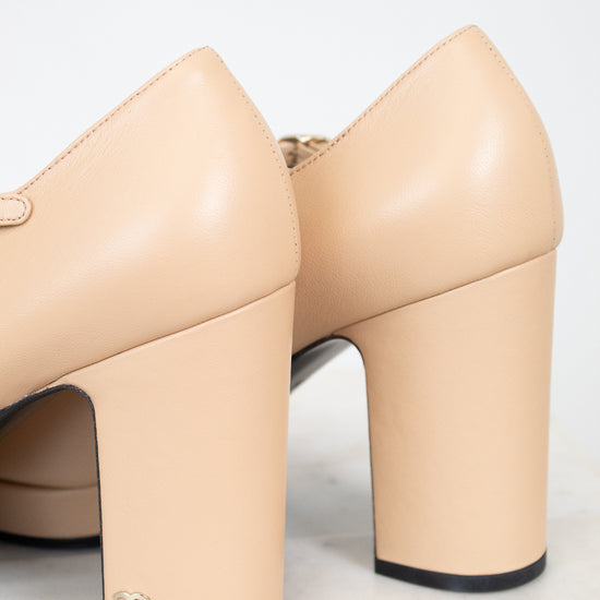 Beige high-heeled shoes with a visible "CC" Chanel brand logo on a light gray background
