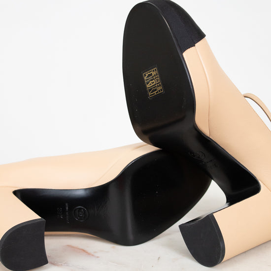 Pair of beige high-heeled shoes with black soles on a light background