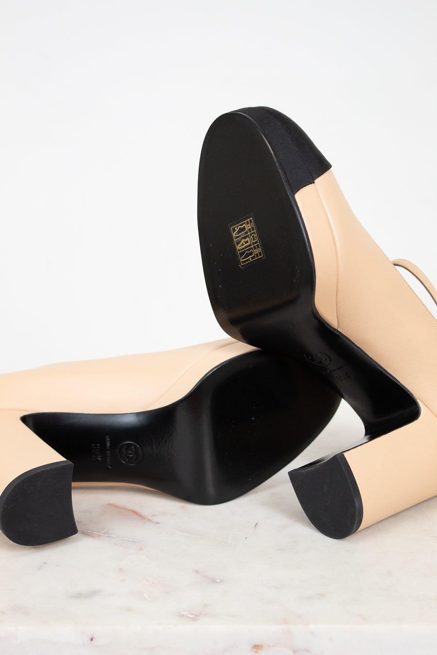 Pair of beige high-heeled shoes with black soles on a light background