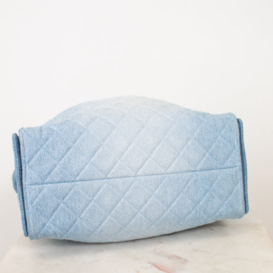 A light blue quilted fabric cover or pouch with a diamond stitched pattern, resting on a white marble surface against a plain white background.