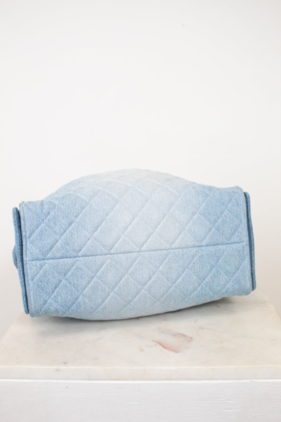 A light blue quilted fabric cover or pouch with a diamond stitched pattern, resting on a white marble surface against a plain white background.