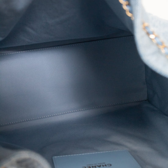 Close-up of the interior of a Chanel handbag in a muted blue-gray color, showing the branded CHANEL interior card and a gold-tone chain strap.