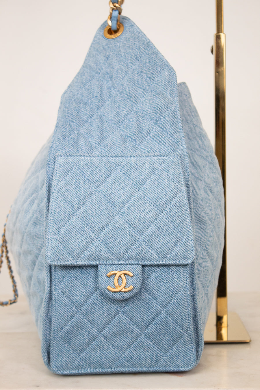 A light blue quilted denim shoulder bag with a gold-tone interlocking CC logo on the front flap, displayed against a light background.