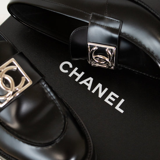 Black Chanel shoes with silver buckles on a black box.