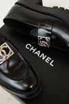 Black Chanel shoes with silver buckles on a black box.
