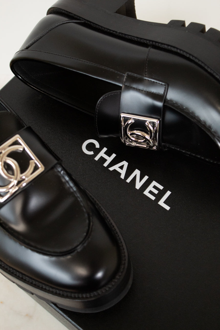 Black Chanel shoes with silver buckles on a black box.