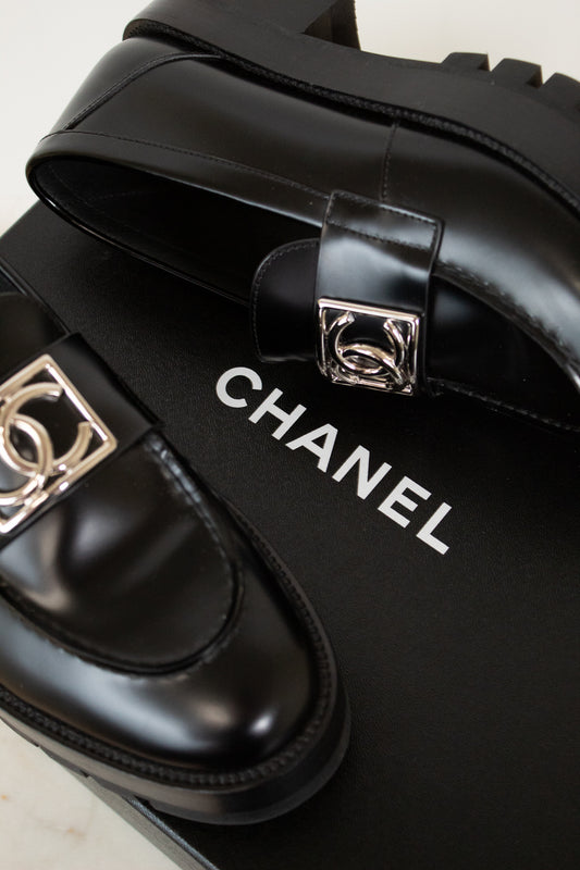 Black Chanel shoes with silver buckles on a black box.