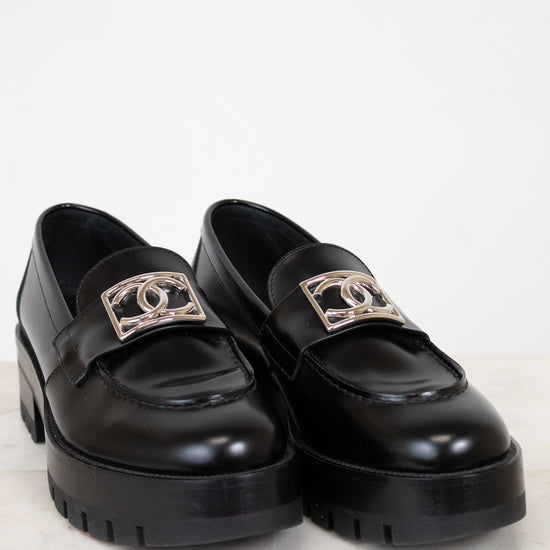 Black loafers with gold logo accents on a light background
