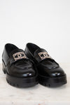 Black loafers with gold logo accents on a light background