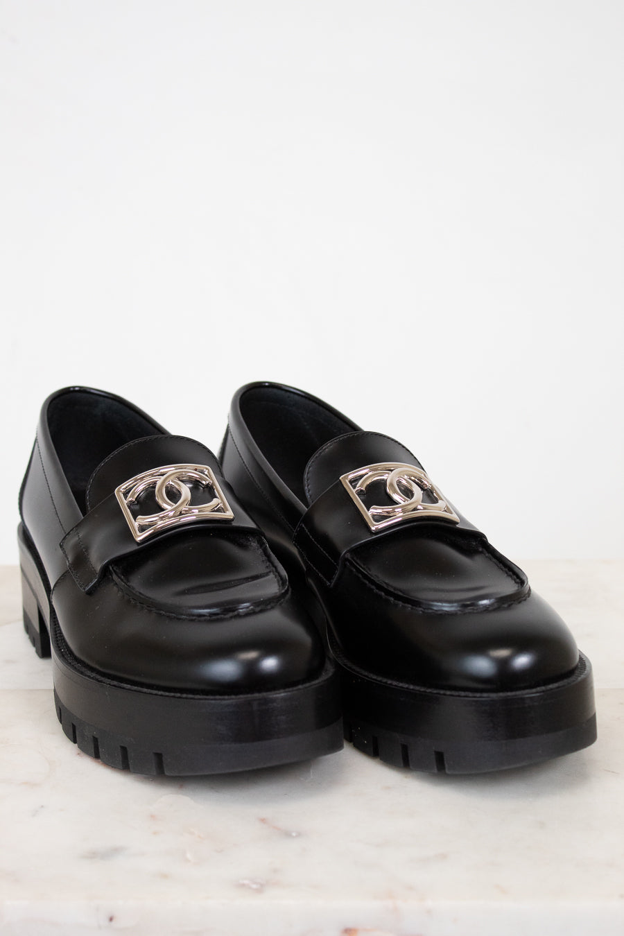 Black loafers with gold logo accents on a light background