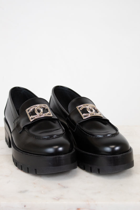 Black loafers with gold logo accents on a light background