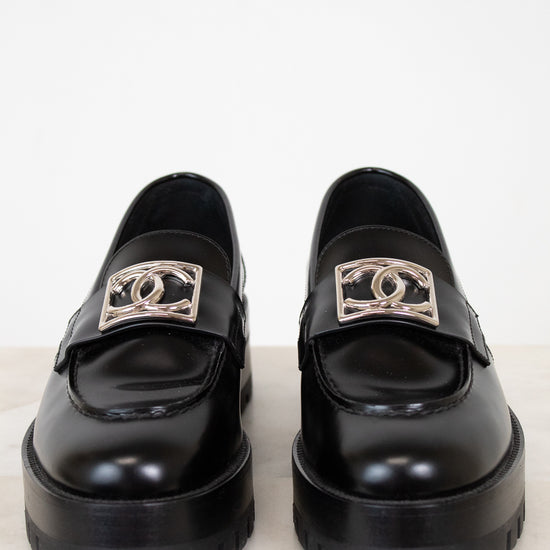 Pair of black loafers with silver CC logo on a white background