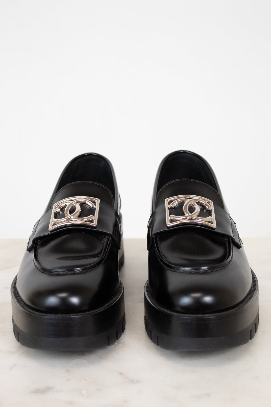 Pair of black loafers with silver CC logo on a white background