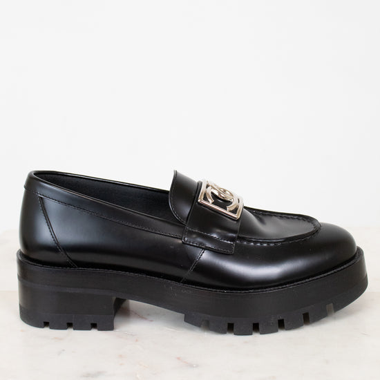Black loafer shoe with a silver logo detail on a light background