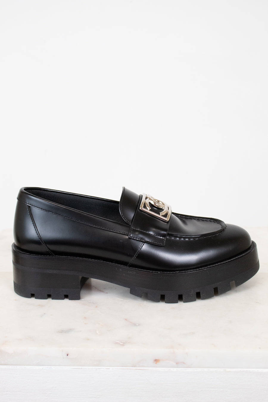 Black loafer shoe with a silver logo detail on a light background