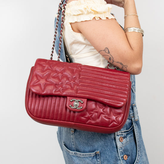 Person holding a red quilted handbag with a visible brand logo against a plain background