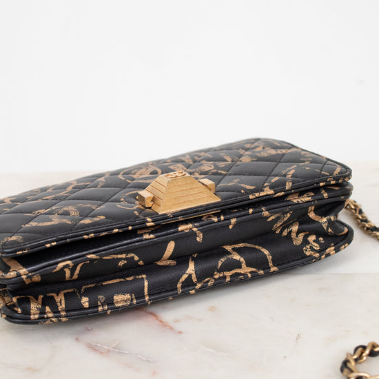 Black quilted handbag with gold chain strap on a white marble surface