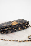 Black quilted handbag with gold chain strap on a white marble surface