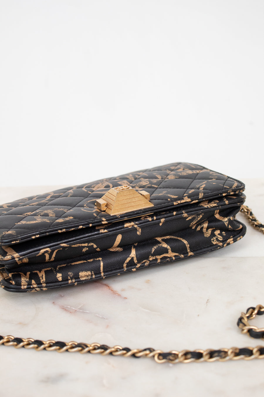 Black quilted handbag with gold chain strap on a white marble surface