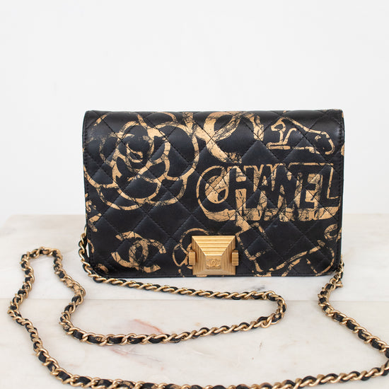 Black quilted handbag with gold chain strap and 'Chanel' branding on a white marble surface.