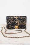 Black quilted handbag with gold chain strap and 'Chanel' branding on a white marble surface.