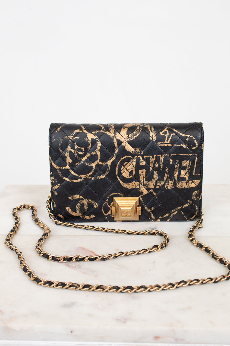Black quilted handbag with gold chain strap and 'Chanel' branding on a white marble surface.