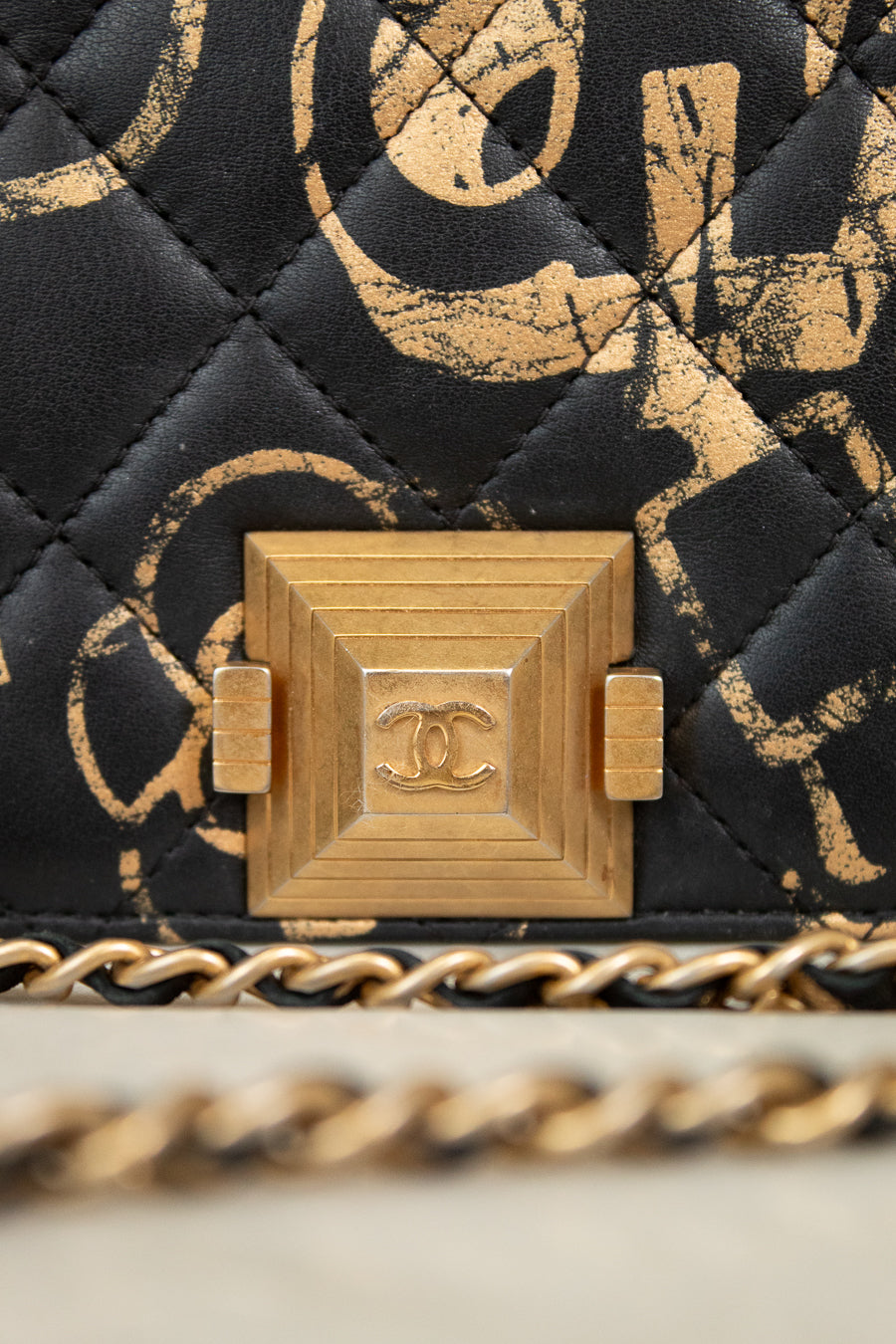 Close-up of a Chanel handbag with gold chain and quilted black and gold pattern.