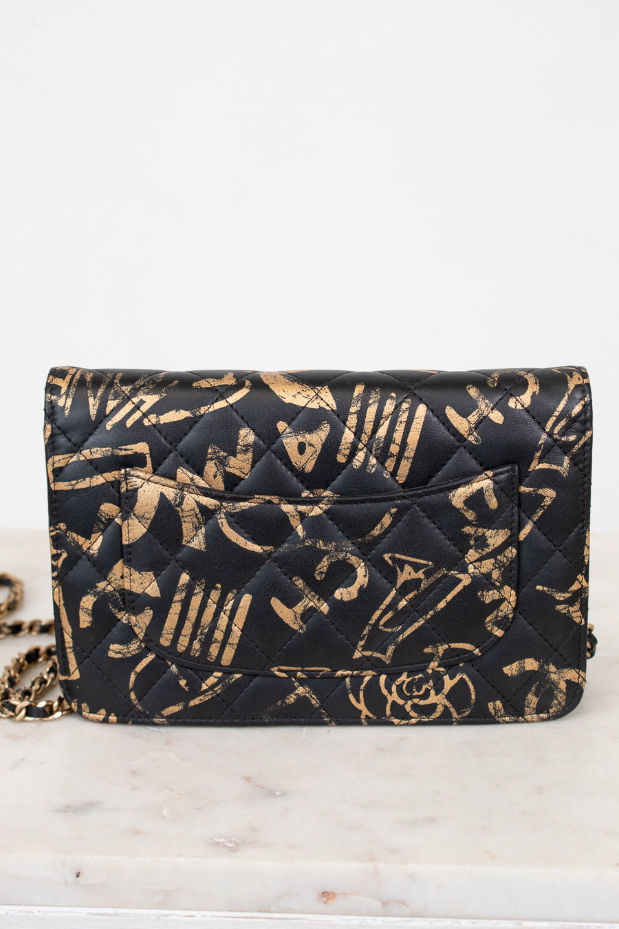 Black quilted handbag with gold lettering on a white marble surface