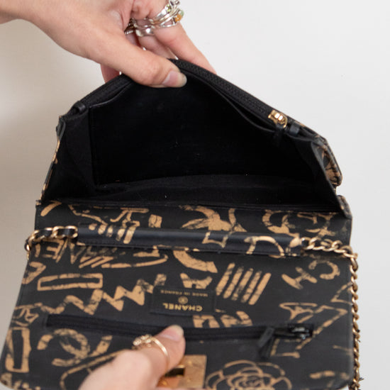 Black handbag with gold patterns held open by a hand on a white background