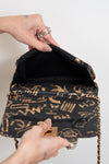 Black handbag with gold patterns held open by a hand on a white background