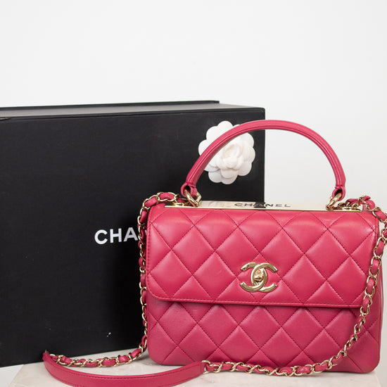 Pink quilted handbag with gold chain and clasp on a white surface with a black box in the background.