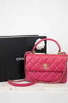 Pink quilted handbag with gold chain and clasp on a white surface with a black box in the background.