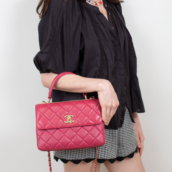 Woman holding a pink quilted handbag with a gold clasp against a plain background