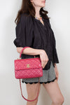 Woman holding a pink quilted handbag with a gold clasp against a plain background