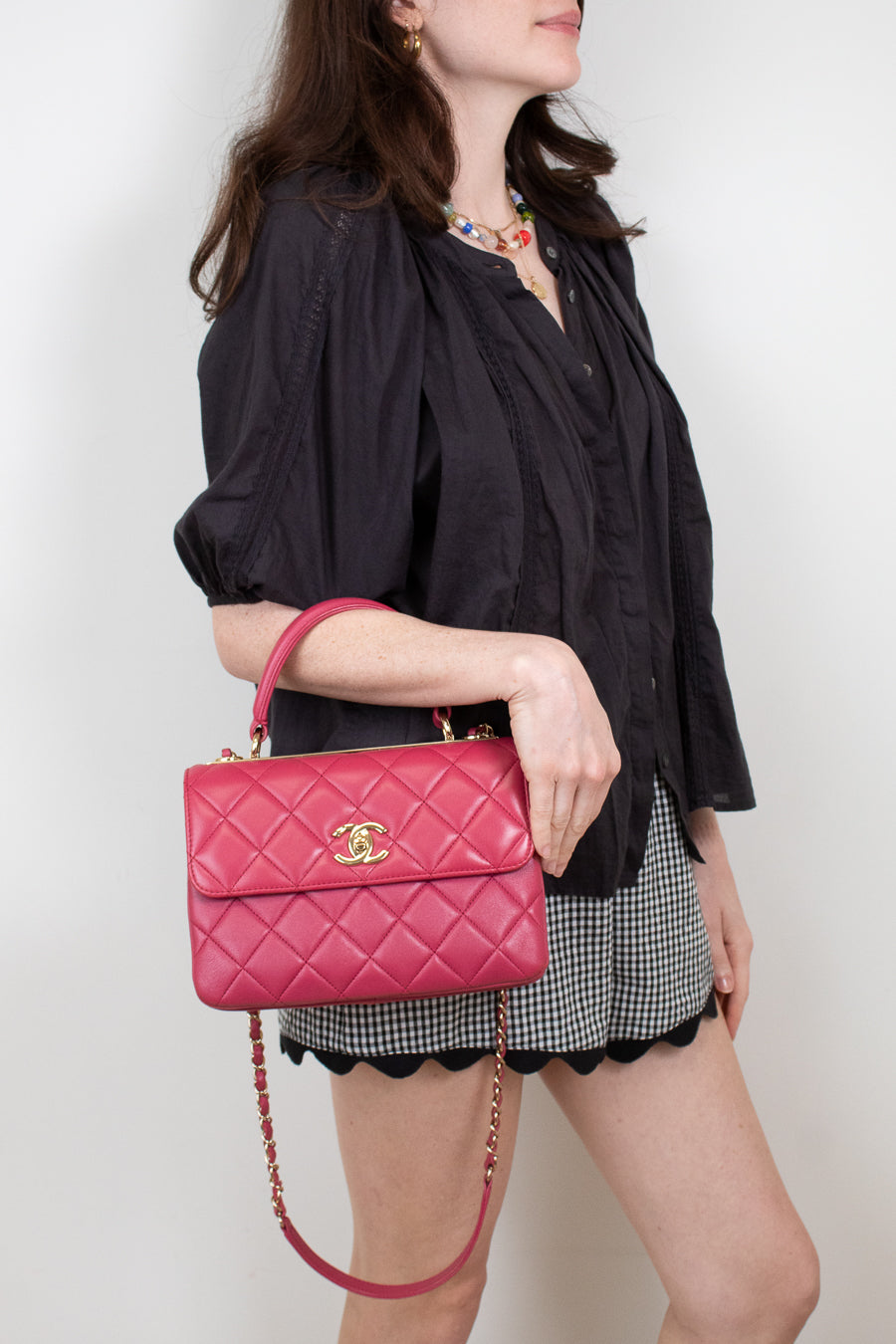 Woman holding a pink quilted handbag with a gold clasp against a plain background