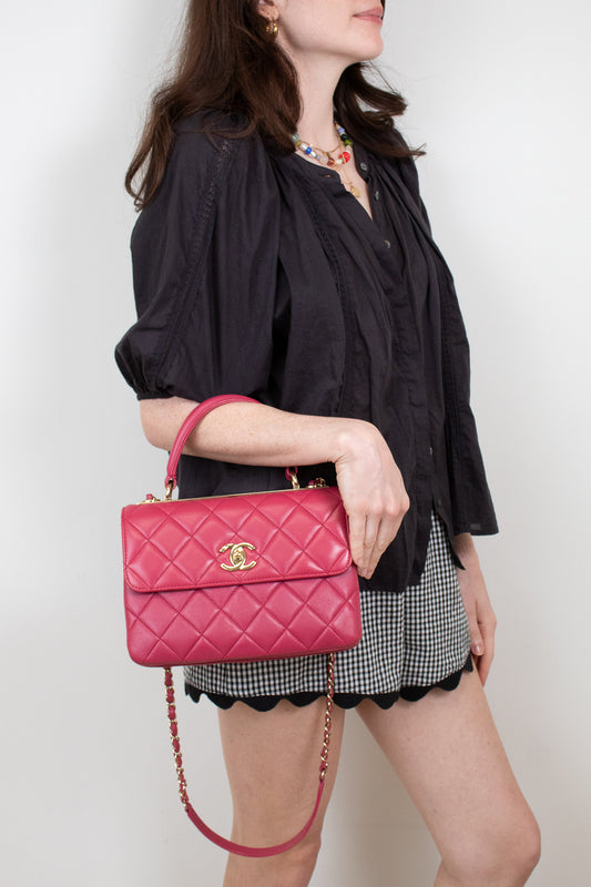 Woman holding a pink quilted handbag with a gold clasp against a plain background
