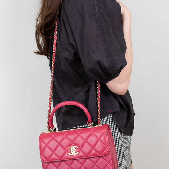 Person holding a pink quilted handbag with a visible brand logo against a plain background
