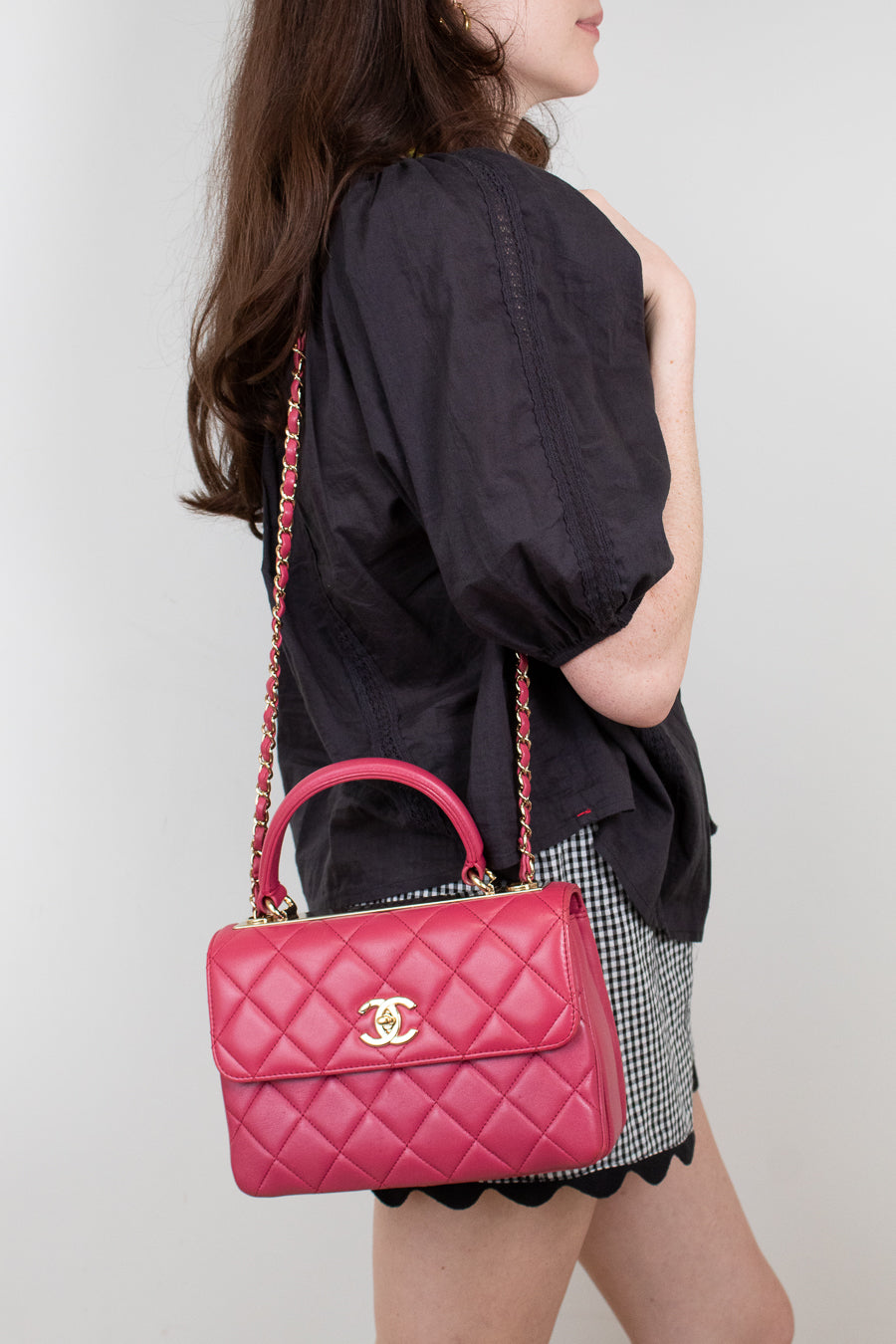 Person holding a pink quilted handbag with a visible brand logo against a plain background