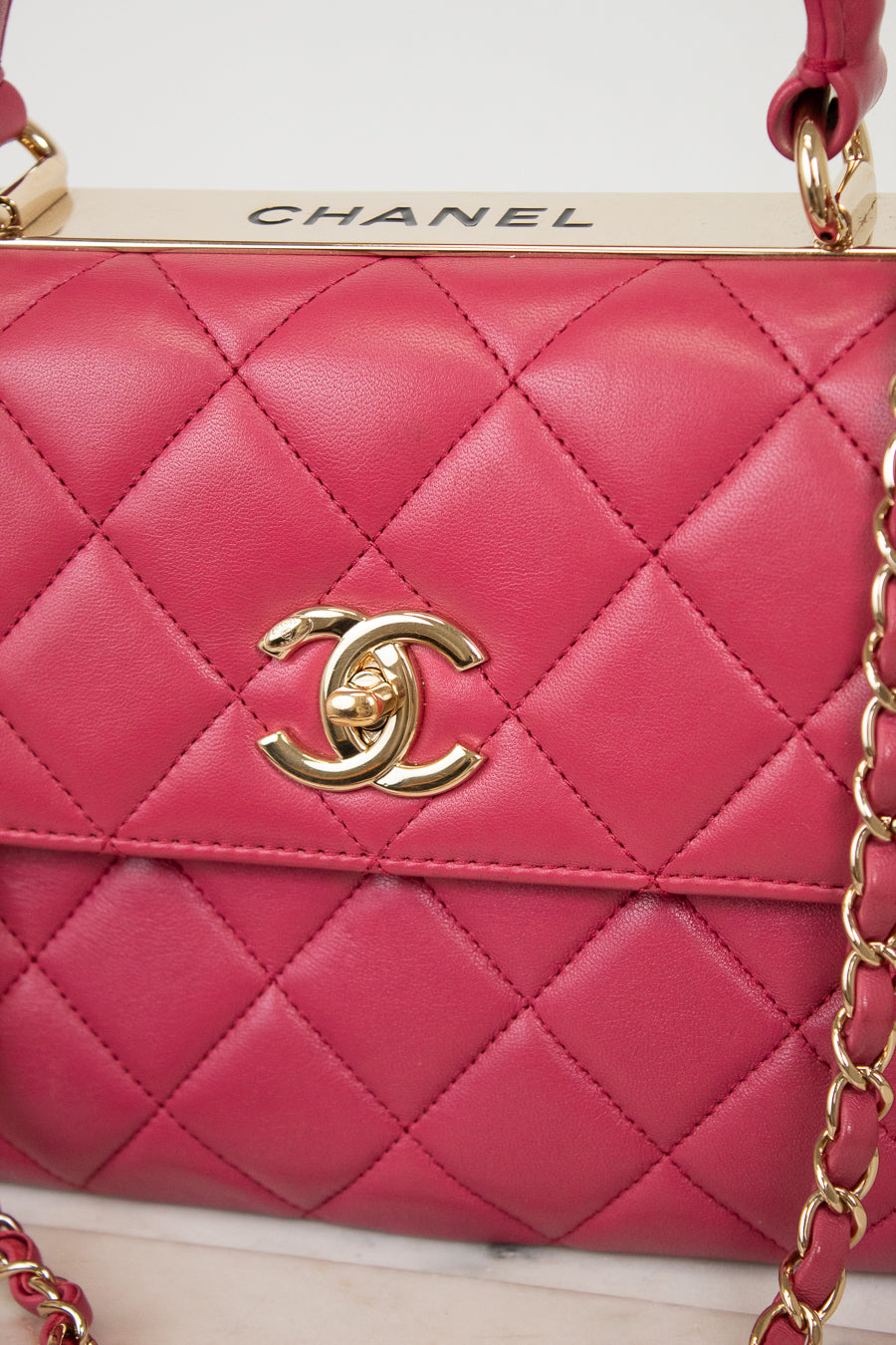 Pink quilted handbag with gold chain and Chanel logo on a white background
