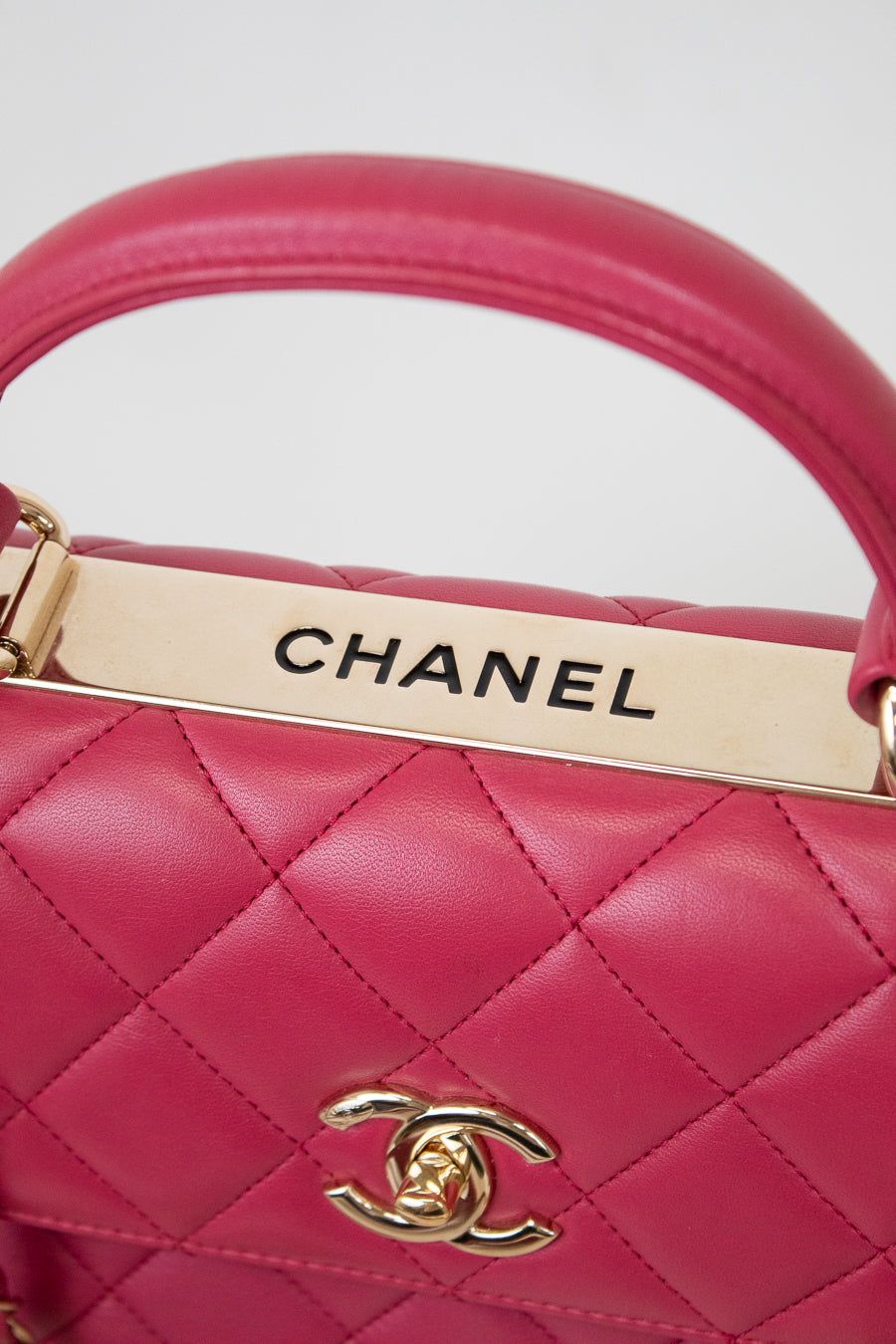 Close-up of a pink Chanel handbag with gold hardware on a light gray background