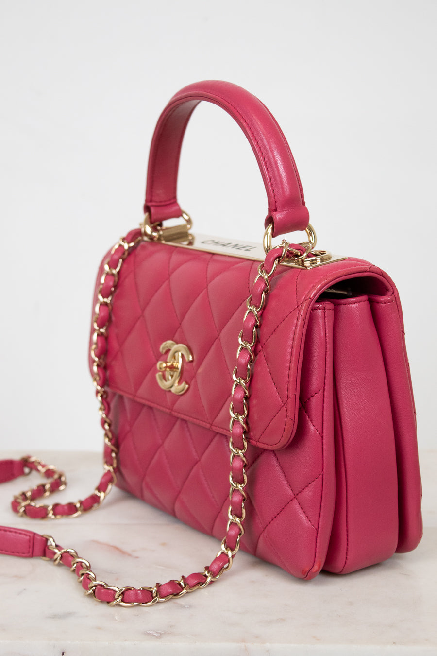 Pink quilted handbag with gold chain and hardware on a light background