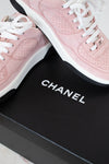 A pair of Chanel low-top sneakers in light pink suede with white laces and white midsoles, displayed on a black Chanel shoebox.