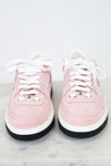 A pair of low-top Chanel sneakers in light pink suede and leather, featuring white laces, white midsoles, black outsoles, and the iconic interlocking CC logo on the tongue.