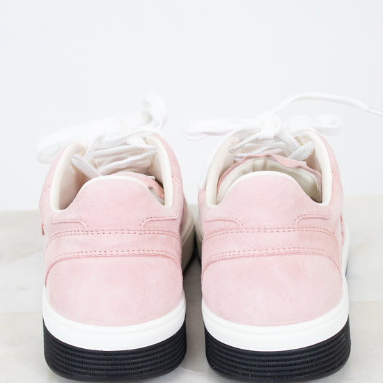 A pair of low-top sneakers shown from the back, featuring light pink suede uppers, white laces, a white midsole, and a black rubber outsole, set against a clean white background.